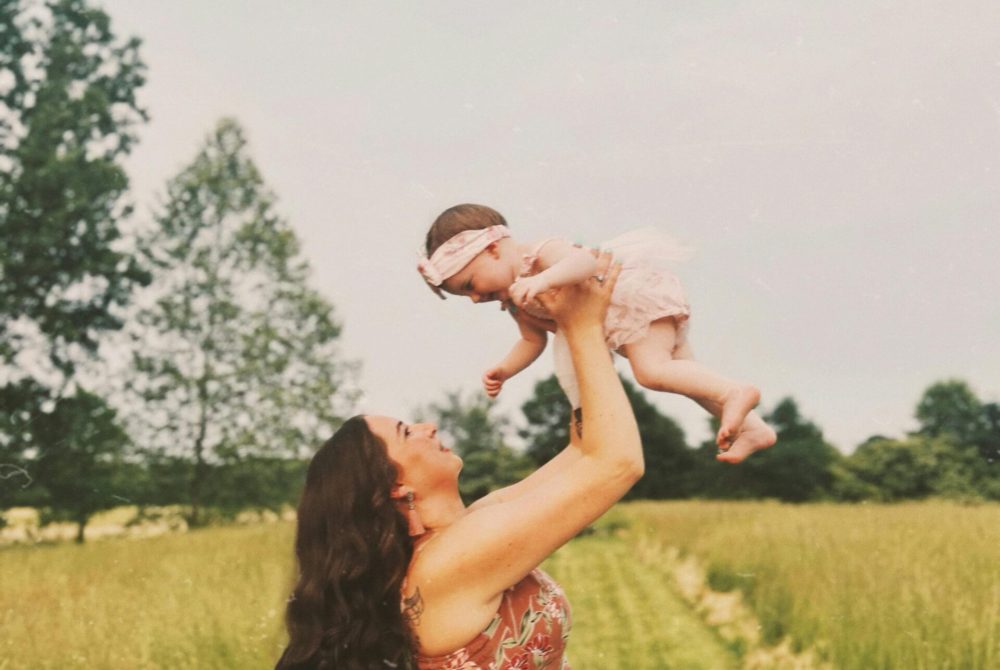 Mother lifting her baby in a sunny field, evokes love and joy.